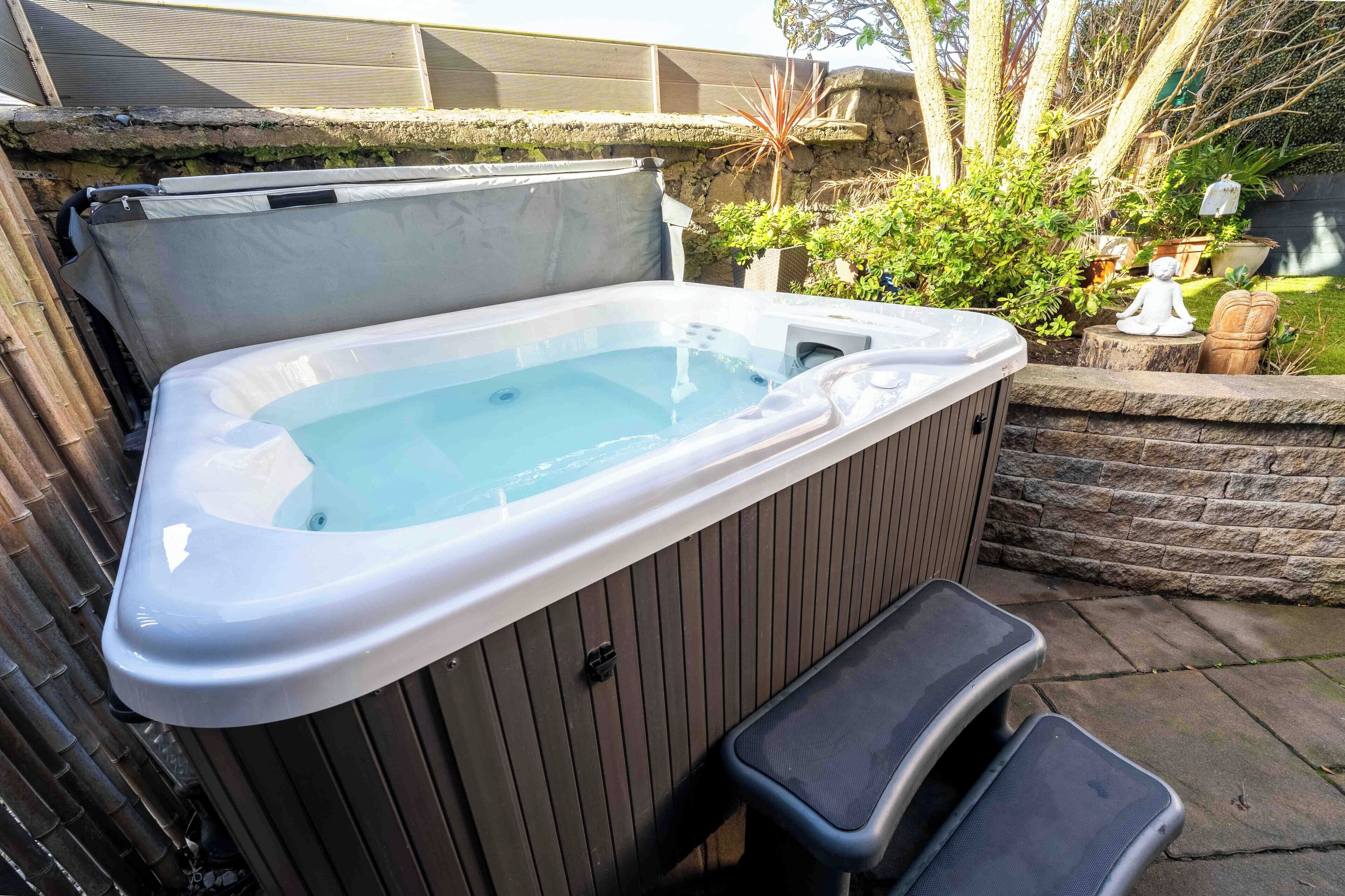 A hot tub with a bench, surrounded by a stone wall and greenery.