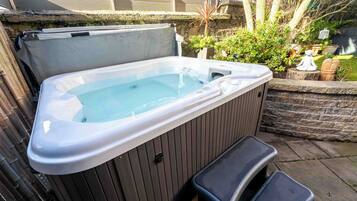 A hot tub with a bench, surrounded by a stone wall and greenery.