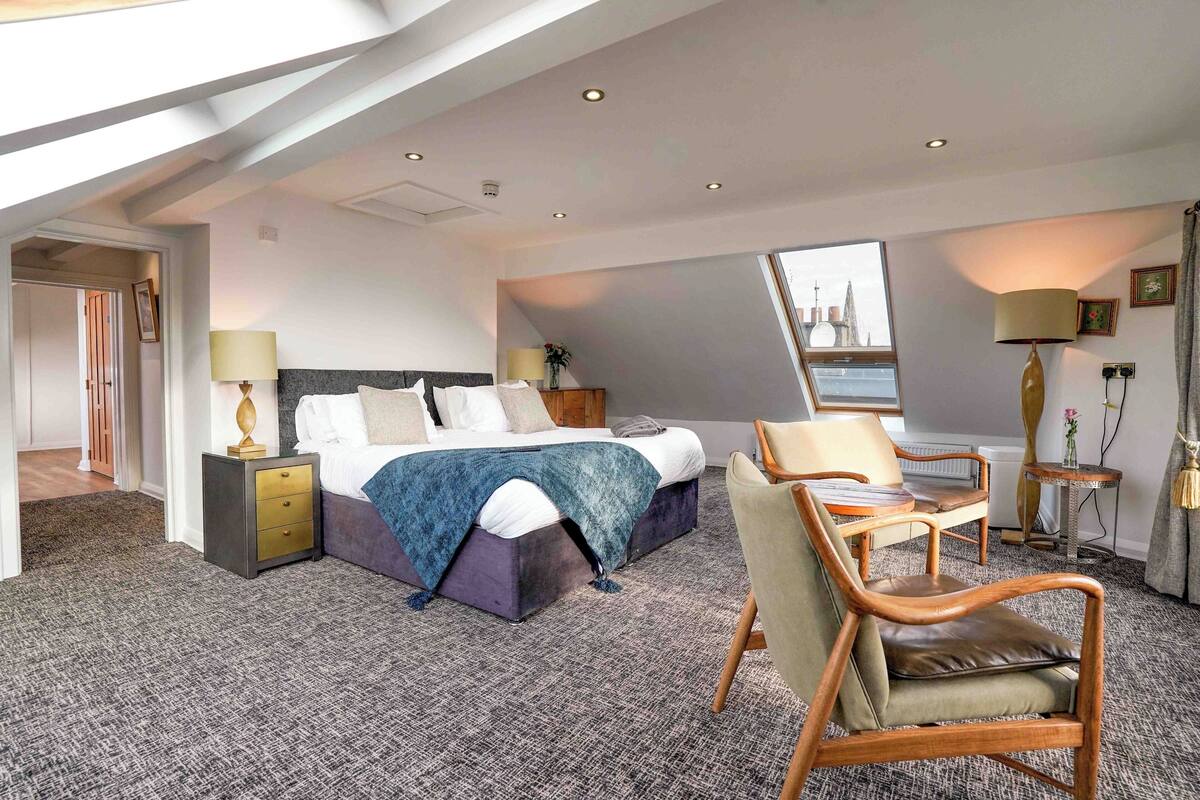 Une chambre d’hôtel avec un lit, une chaise, une table de chevet, une lampe et une vue sur le paysage urbain par la fenêtre.