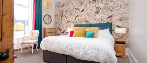 A bedroom with a large bed, a chair, a dresser, and a window with curtains.
