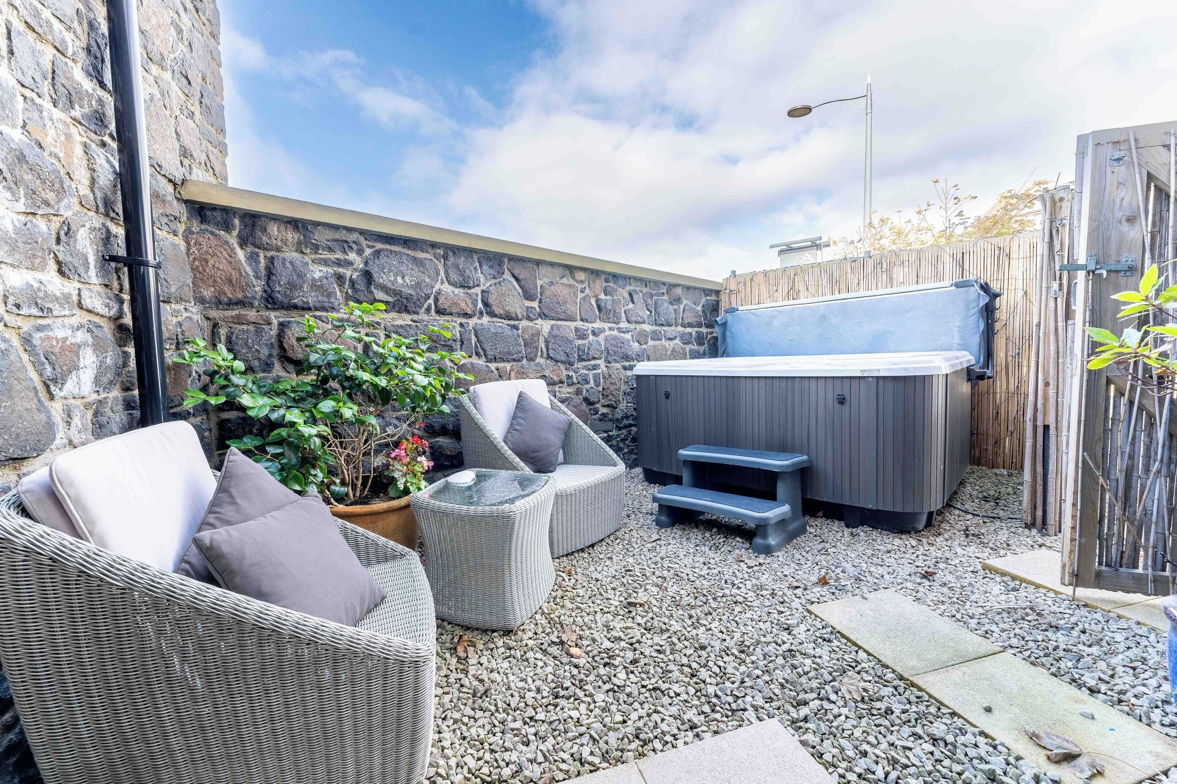 An outdoor patio with wicker furniture, a hot tub, and a stone wall.