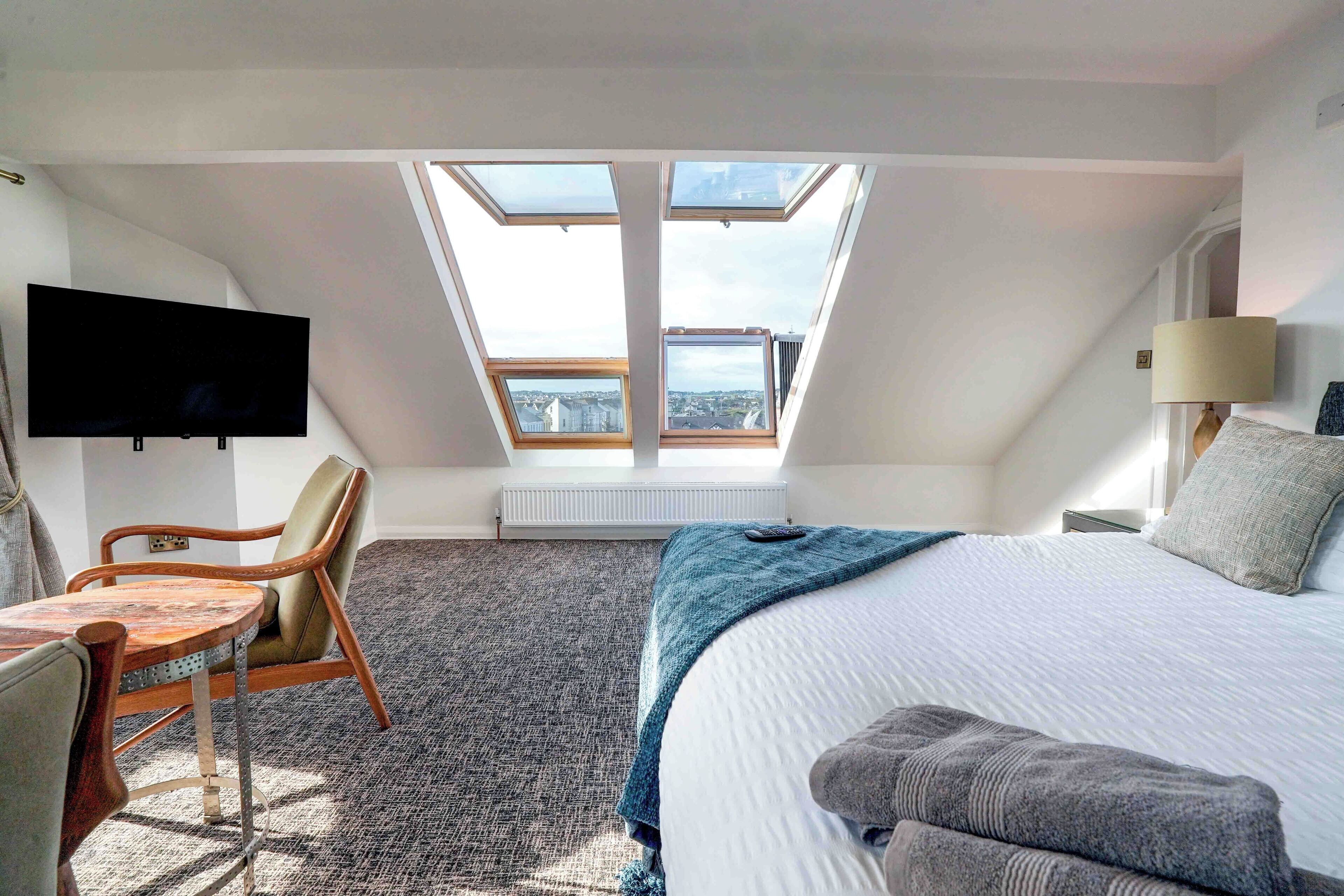 A bedroom with a skylight, a bed, a desk, and a chair.