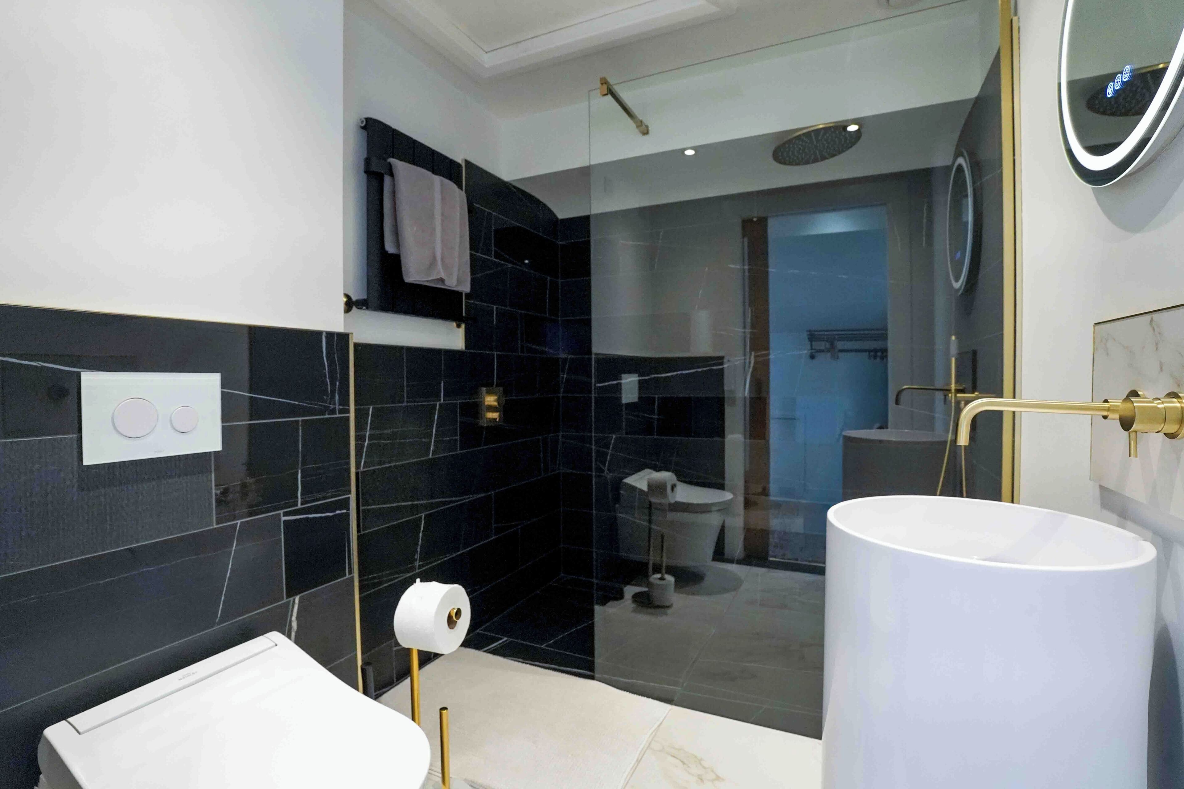 A modern bathroom with a large white sink, a glass shower enclosure, and a toilet visible through the glass.