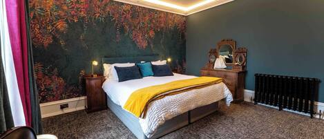 Ein Schlafzimmer mit einem großen Bett, einem Nachttisch, einer Kommode, einem Heizkörper und einem Spiegel.