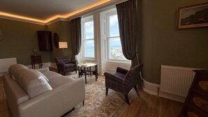 A living room with a sofa, two armchairs, a small table, and a view of the sea through large windows. - Antrim House Guest Rooms & Suites (Portrush)