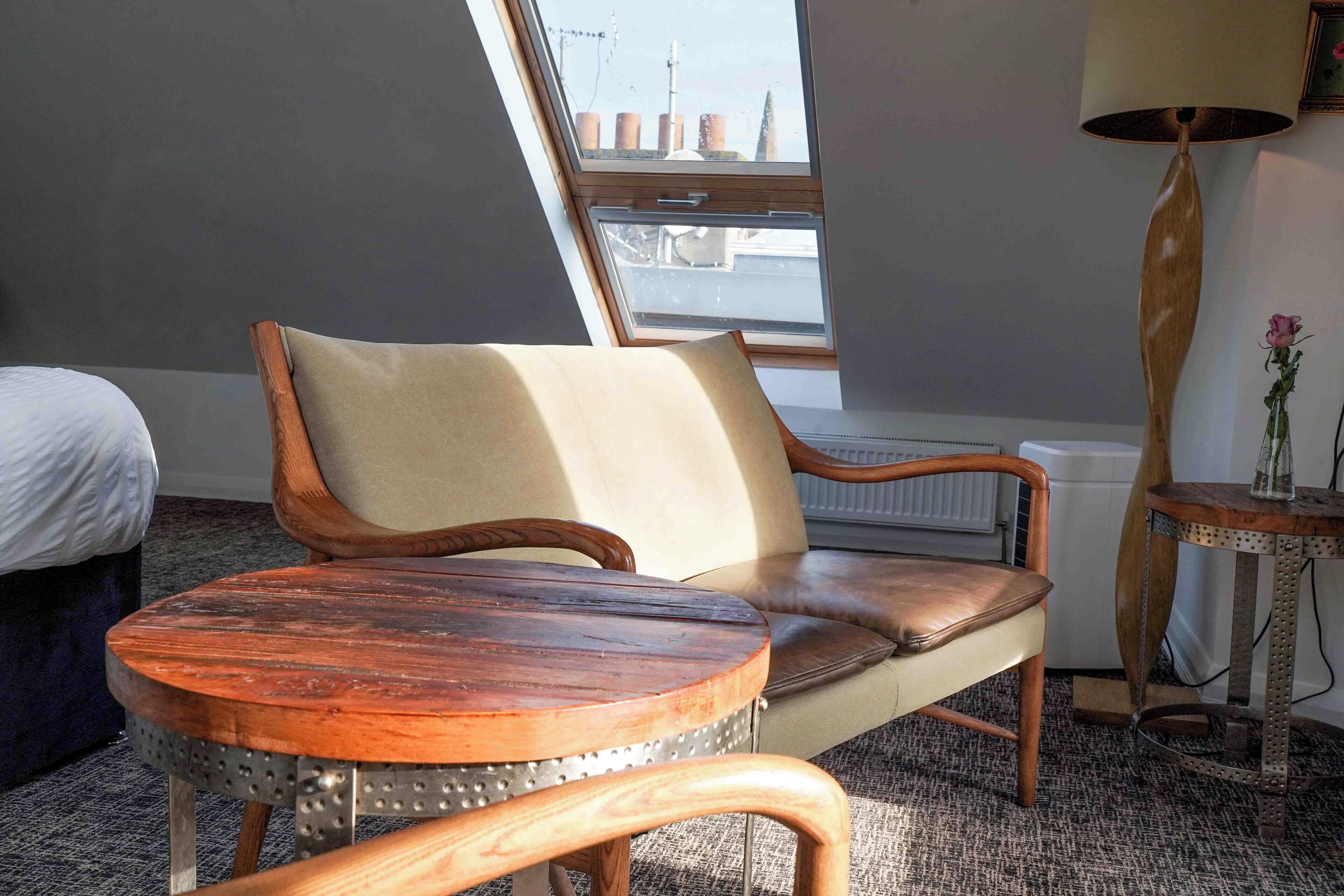 A room with a wooden chair, a round table, a window with a view, a radiator, and a lamp.