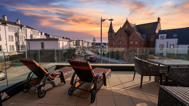 A terrace with wicker furniture, a view of a town, and a sunset. - Antrim House Guest Rooms & Suites (Portrush)
