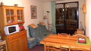 A cozy living room with a wooden dining table, a blue sofa, and a wooden cabinet with glass doors. - LE PLEYNET, LES 7 LAUX, studio cabin 4 people (Le Pleynet)