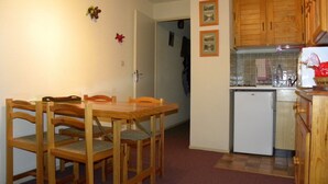 A compact kitchen with wooden cabinets, a white refrigerator, and a dining table with chairs. - LE PLEYNET, LES 7 LAUX, studio cabin 4 people (Le Pleynet)