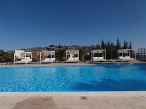 Une piscine entourée de chaises longues blanches, avec un paysage rocheux en arrière-plan.