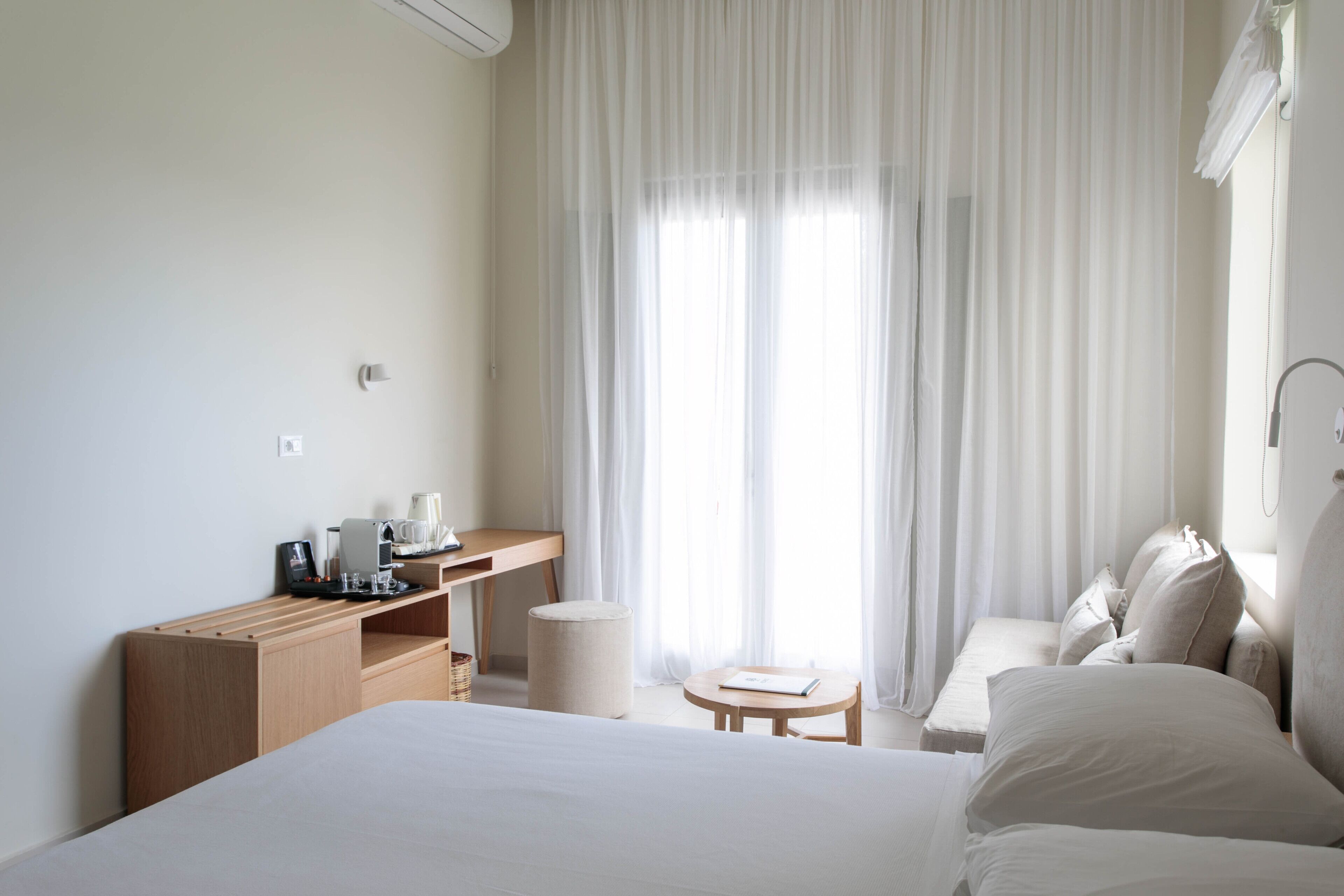 Una habitación de hotel con una cama grande, un escritorio de madera con cafetera, una mesita redonda pequeña y un sofá.
