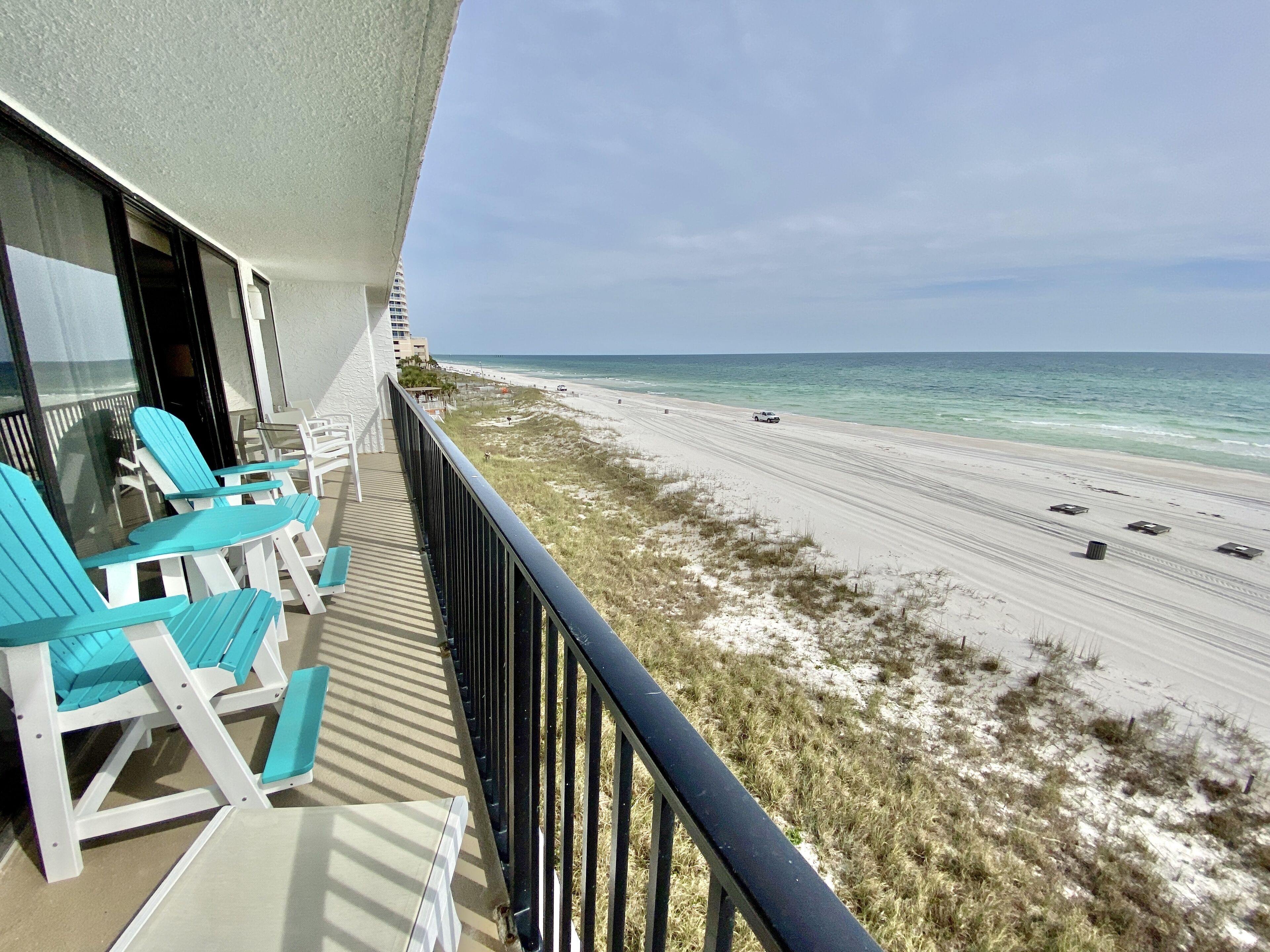 A balcony with turquoise chairs overlooking a beach with a clear view of the ocean.