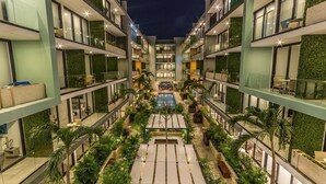 A multi-story hotel with a central courtyard featuring a swimming pool, surrounded by lush greenery and modern architecture. - Beautiful Menesse the city, Delux Apartment (Playa del Carmen)