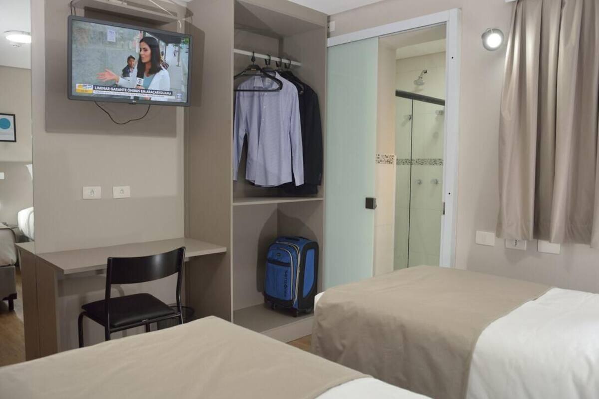 A hotel room with a TV, a desk, two beds, a wardrobe, and a suitcase.