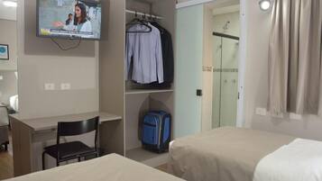 A hotel room with a TV, a desk, a chair, a wardrobe, and a bed.