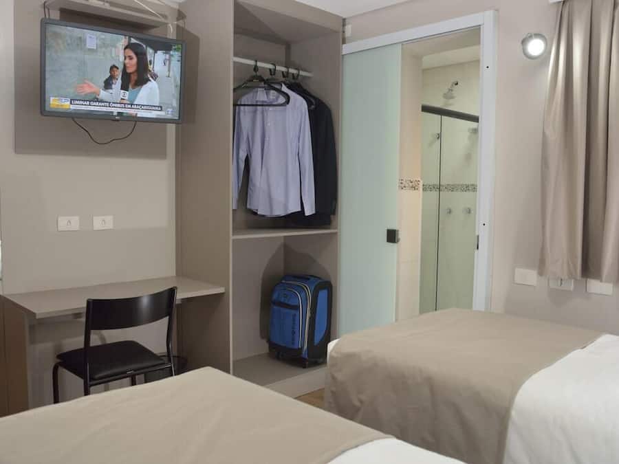 A hotel room with a TV, a desk, a chair, a wardrobe, and a bed.