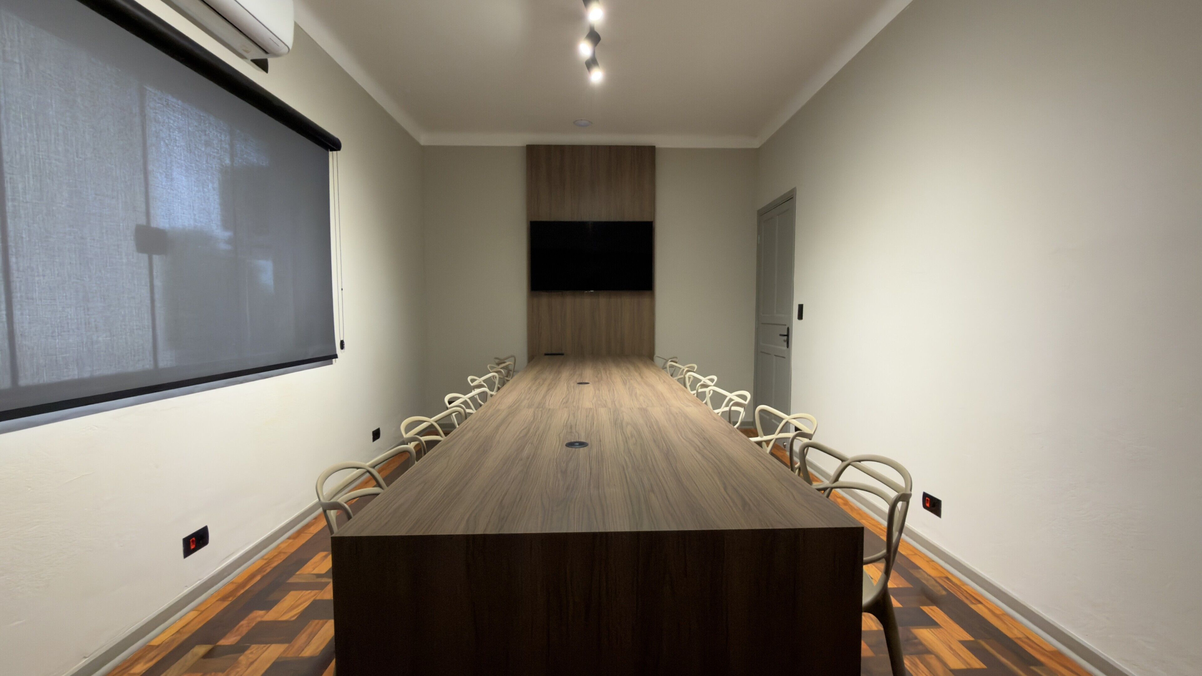 Un salón de conferencias con una mesa larga, sillas, una pantalla de proyector y una puerta.