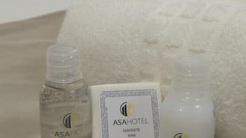 A hotel room with a bed, a laptop, and toiletries including a bottle of shampoo, soap, and conditioner.