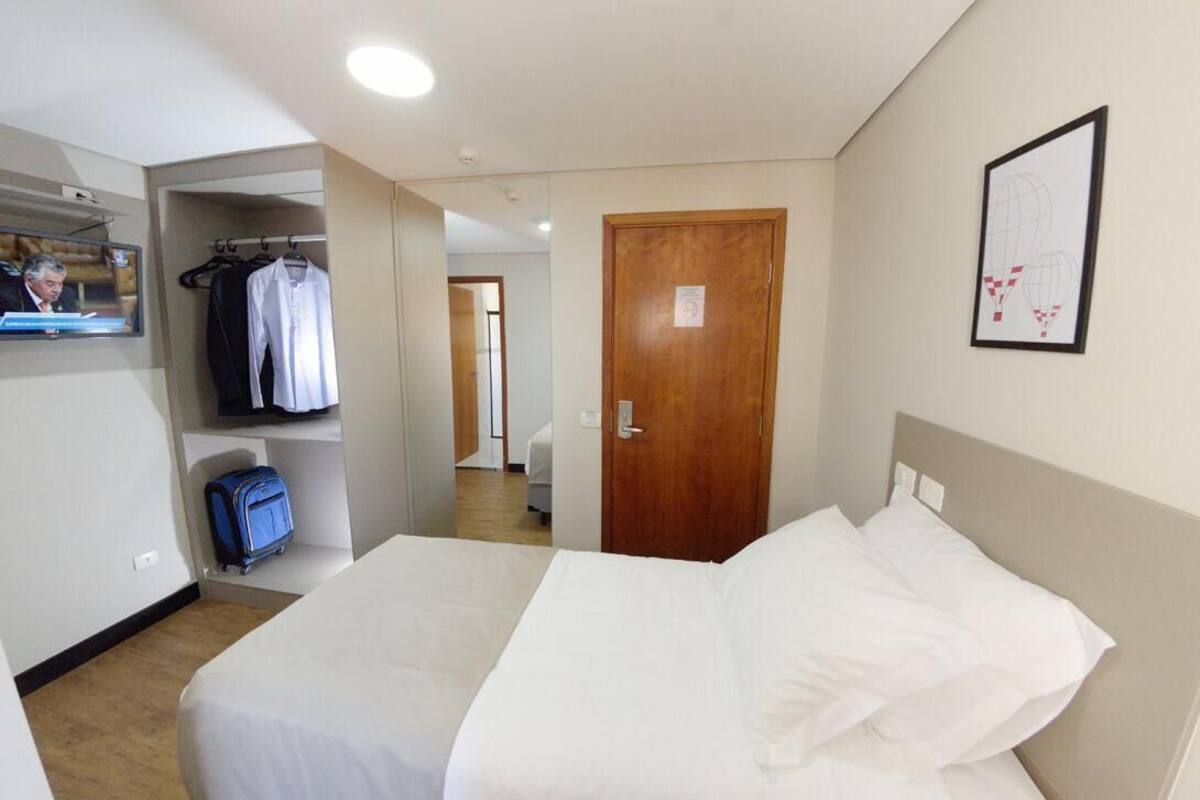 A hotel room with a bed, a wardrobe, a television, and a door.
