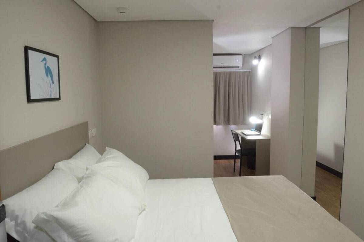 A hotel room with a bed, a desk, and an air conditioning unit.
