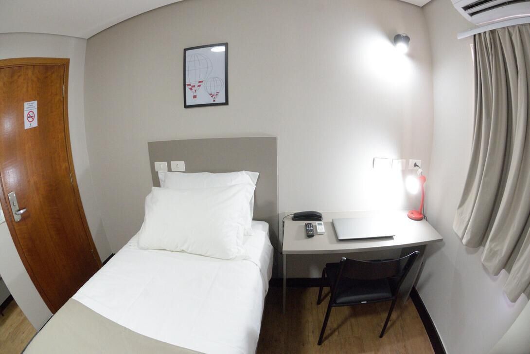 Ein Hotelzimmer mit einem Bett, einem Schreibtisch mit Stuhl, einem Telefon, einer Lampe und einer Tür.