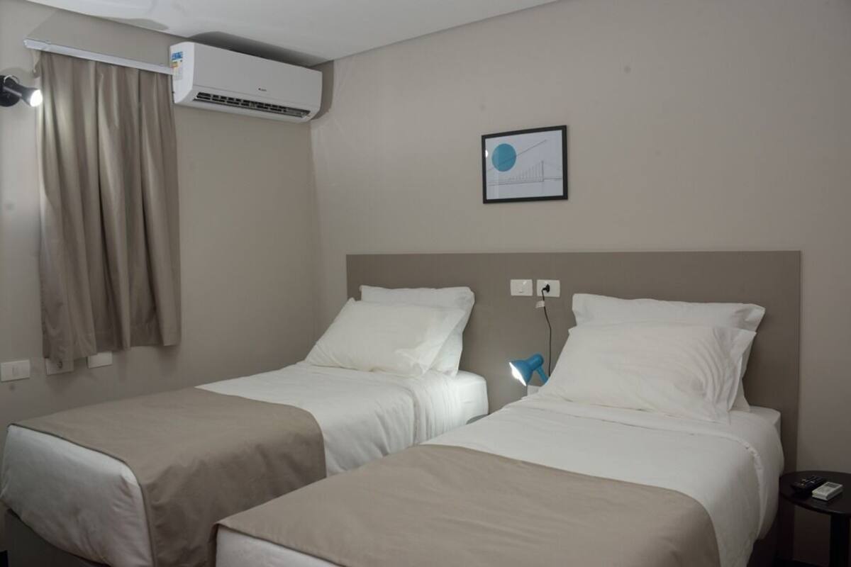 A hotel room with two beds, a ceiling fan, an air conditioning unit, a framed picture on the wall, and a bedside lamp.