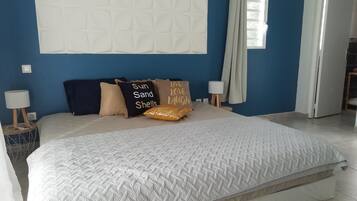 A bedroom with a large bed, a nightstand with a lamp, and a wall-mounted light fixture.