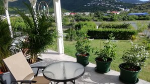 Een terras met een tafel en stoelen, omringd door plantenpotten en een uitzicht op een groen landschap met huizen in de verte.