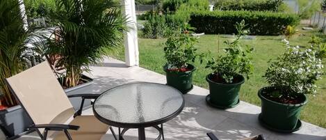 Une terrasse avec une table et des chaises, entourée de plantes en pot et offrant une vue sur un paysage verdoyant, avec des maisons visibles au loin.