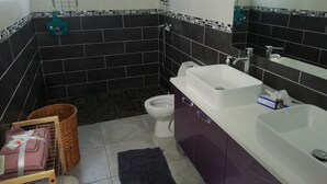 Een badkamer met zwart-wit betegelde wanden, een witte wastafel, een paars badkamermeubel, een wit toilet en een douchehoek.