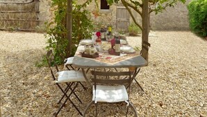 Une table est dressée sous une pergola, avec un mur de pierre et un bâtiment rustique en arrière-plan.