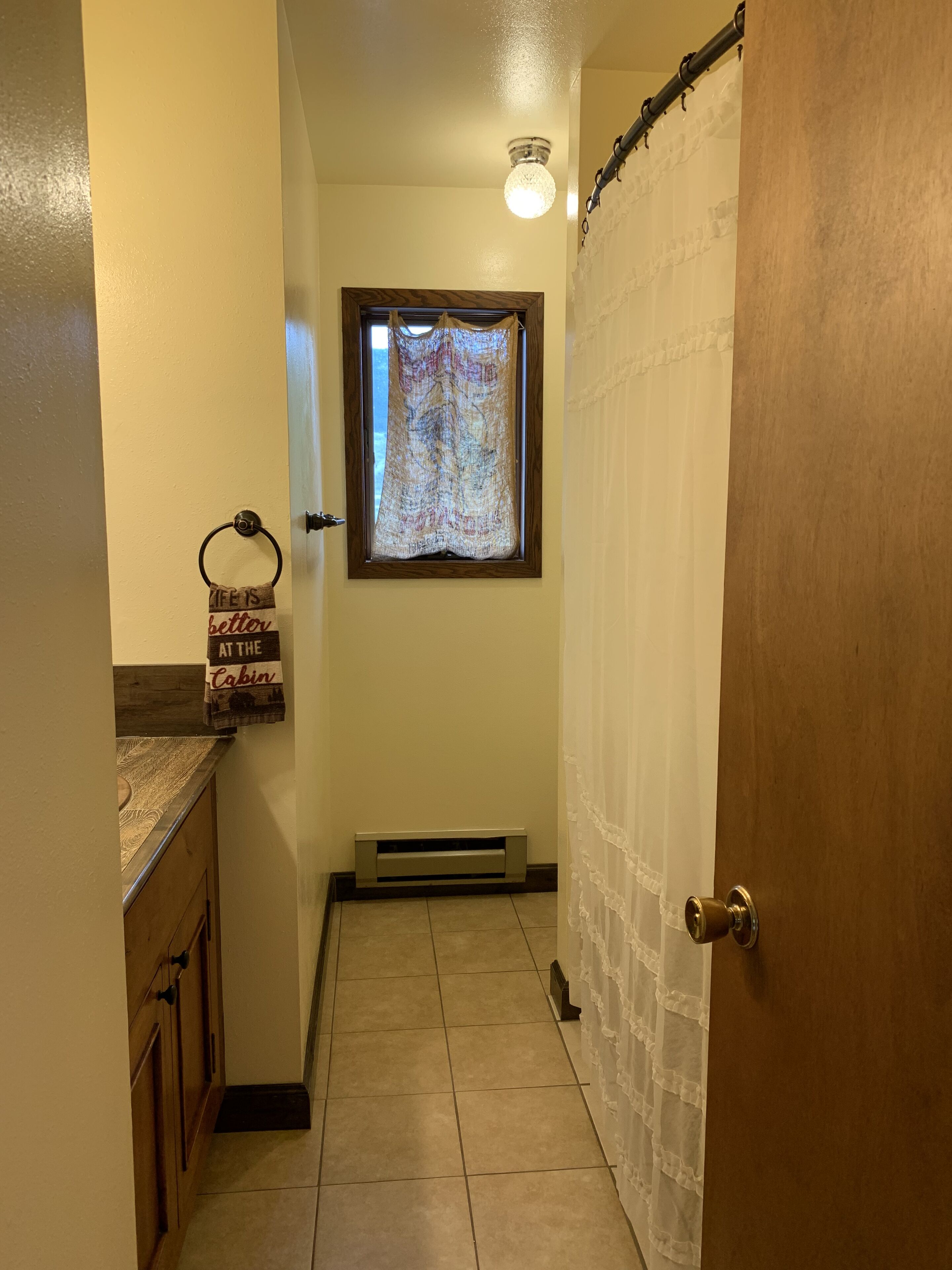 Une petite salle de bain avec un rideau de douche, une fenêtre donnant sur un beau paysage et un porte-serviettes avec une pancarte.