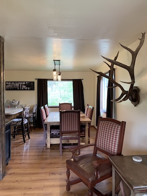 Uma sala de jantar com uma mesa e cadeiras de madeira, um candelabro e um chifre de veado fixado na parede.