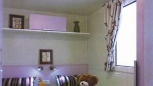 A room with two beds, a window with floral curtains, and a teddy bear on one bed. - Victoria Mobilehome Camping Poljana (Mali Losinj)