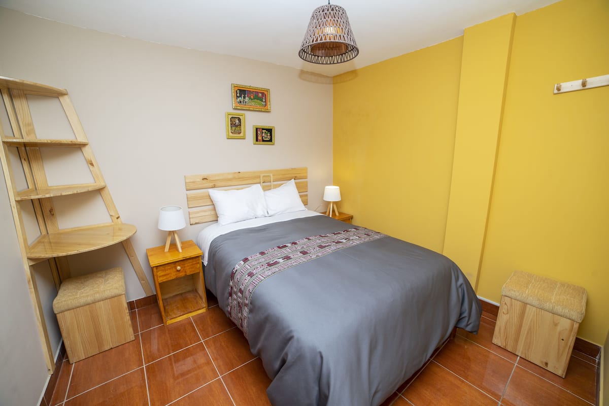 A bedroom with a bed, bedside tables, a wooden ladder, a small stool, and a hanging light fixture.