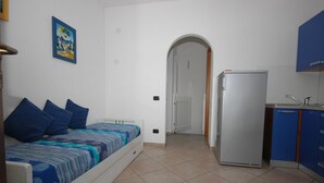 Een kleine kamer met een bed, een koelkast en een kitchenette.