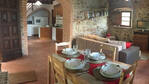 A dining area with a table set for four, a kitchen in the background, and a stone wall. - Villa San Martino (Pomarance)