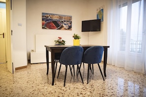 A dining area with a table, two chairs, a potted plant, and a painting on the wall.