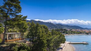 Una casetta sul lungomare con un terrazzo in legno, con vista su una spiaggia e una baia con barche.