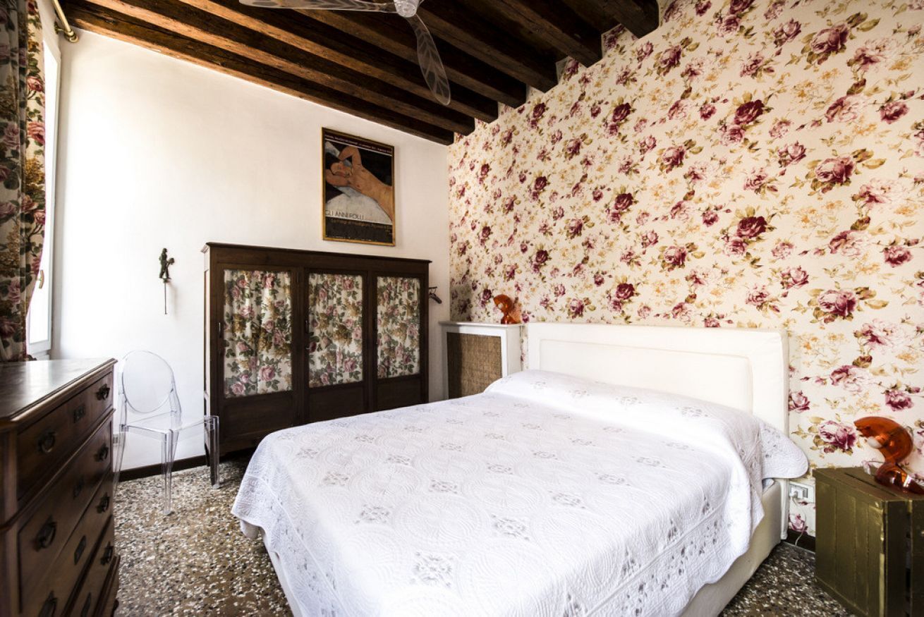 A bedroom with a bed, wooden dresser, and floral wallpaper.