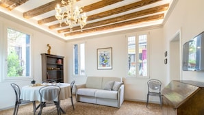 Una habitación con techo de madera, un candelabro, un sofá, una mesa de comedor con sillas y una estantería.