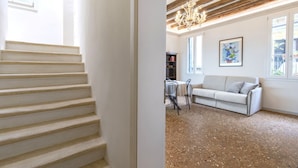 Una escalera conduce a una habitación con un sofá blanco, una araña y un cuadro en la pared.