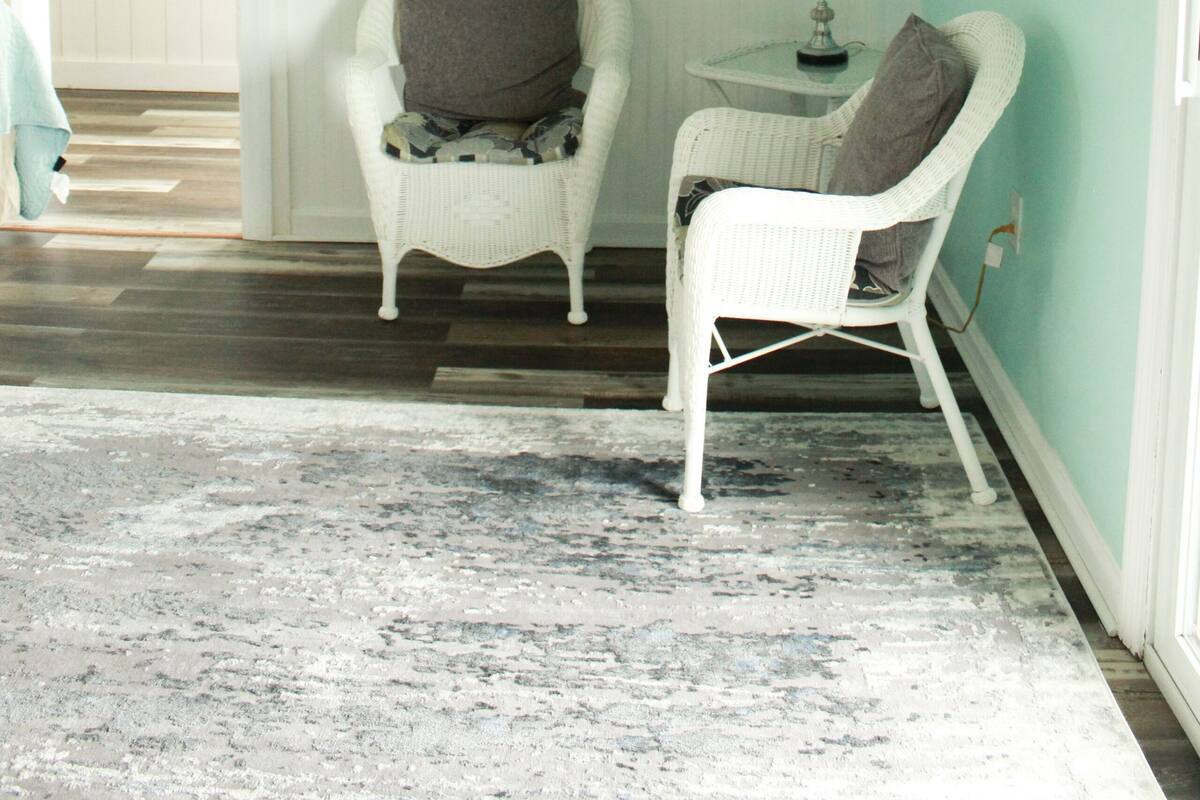 A room with teal walls, two white wicker chairs, a small table with a lamp, and a patterned rug.