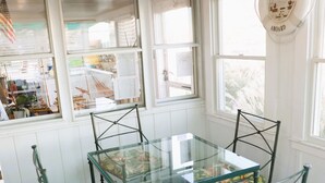 A dining area with a glass table and chairs, white walls, and large windows.