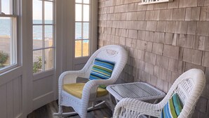 Une pièce avec deux fauteuils en osier dotés de coussins jaunes, un mur en bois sur lequel est inscrit le mot « PLAGE », et de grandes fenêtres donnant sur la mer.