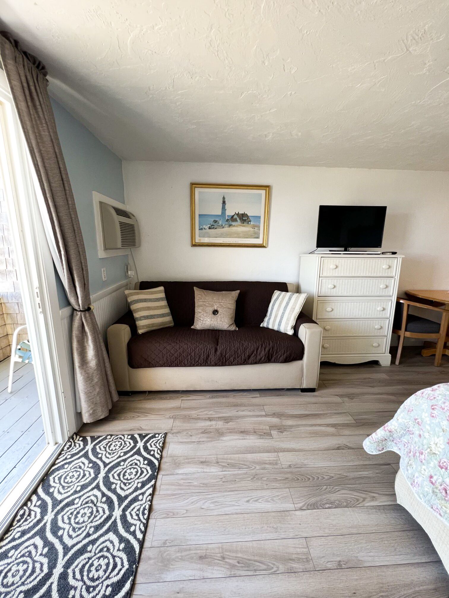 A cozy room with a dark brown sofa, a white dresser, a television, and a framed picture of a lighthouse on the wall.