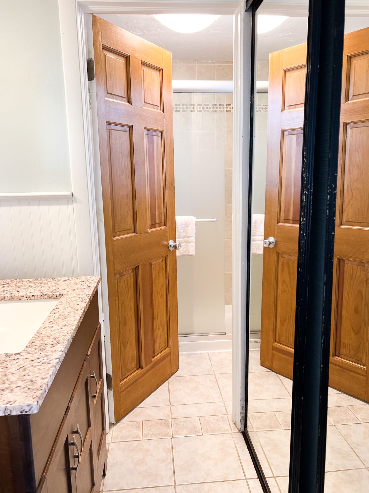 A bathroom with wooden doors, a shower, and a marble countertop.