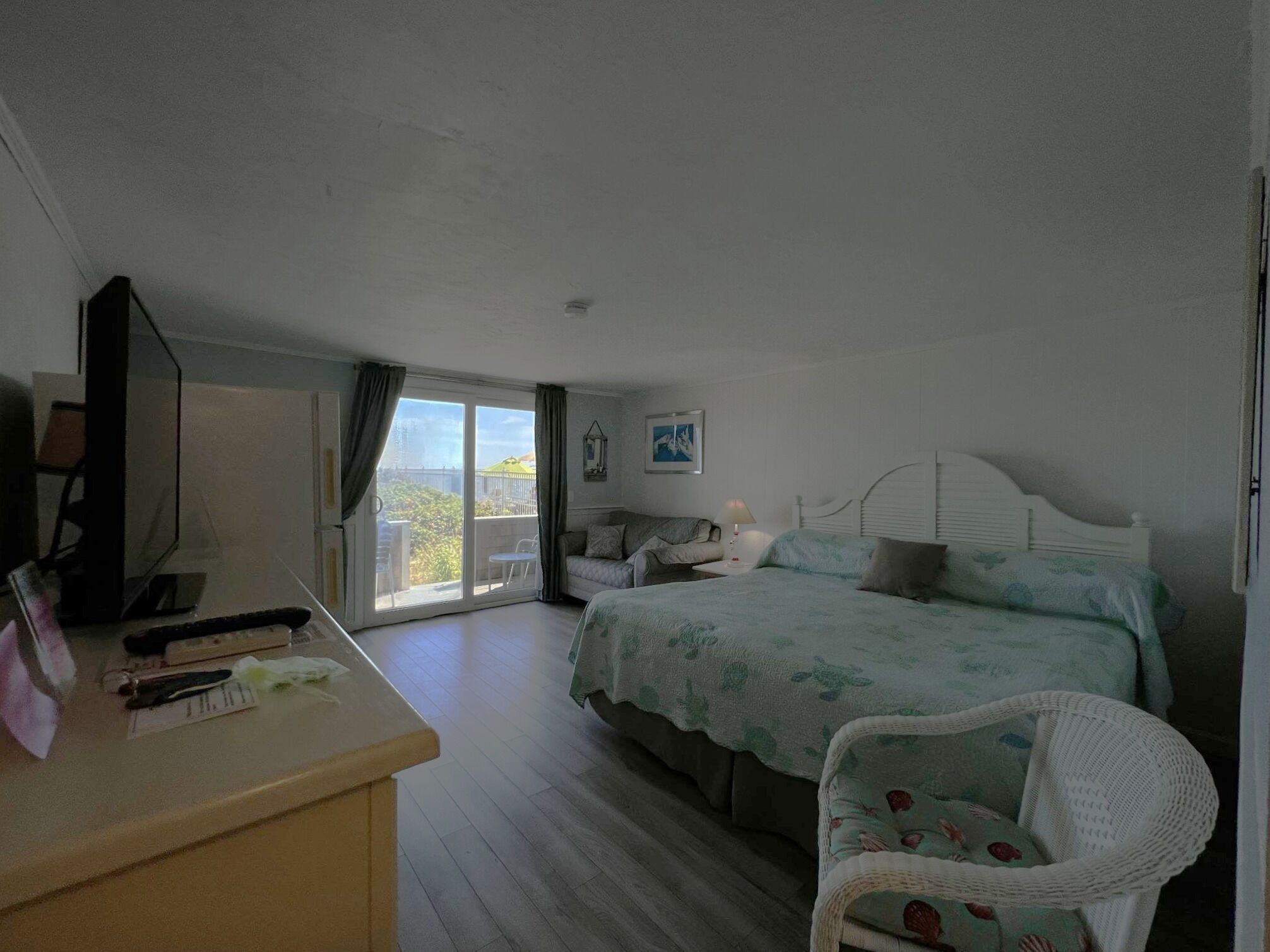 A bedroom with a bed, a desk, a chair, a TV, and a balcony with a view.
