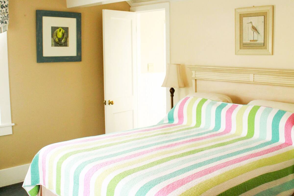 A bedroom with a bed, a door, and a wall with a framed picture.