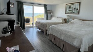 A hotel room with two beds, a desk, a coffee machine, and a view of the sea.